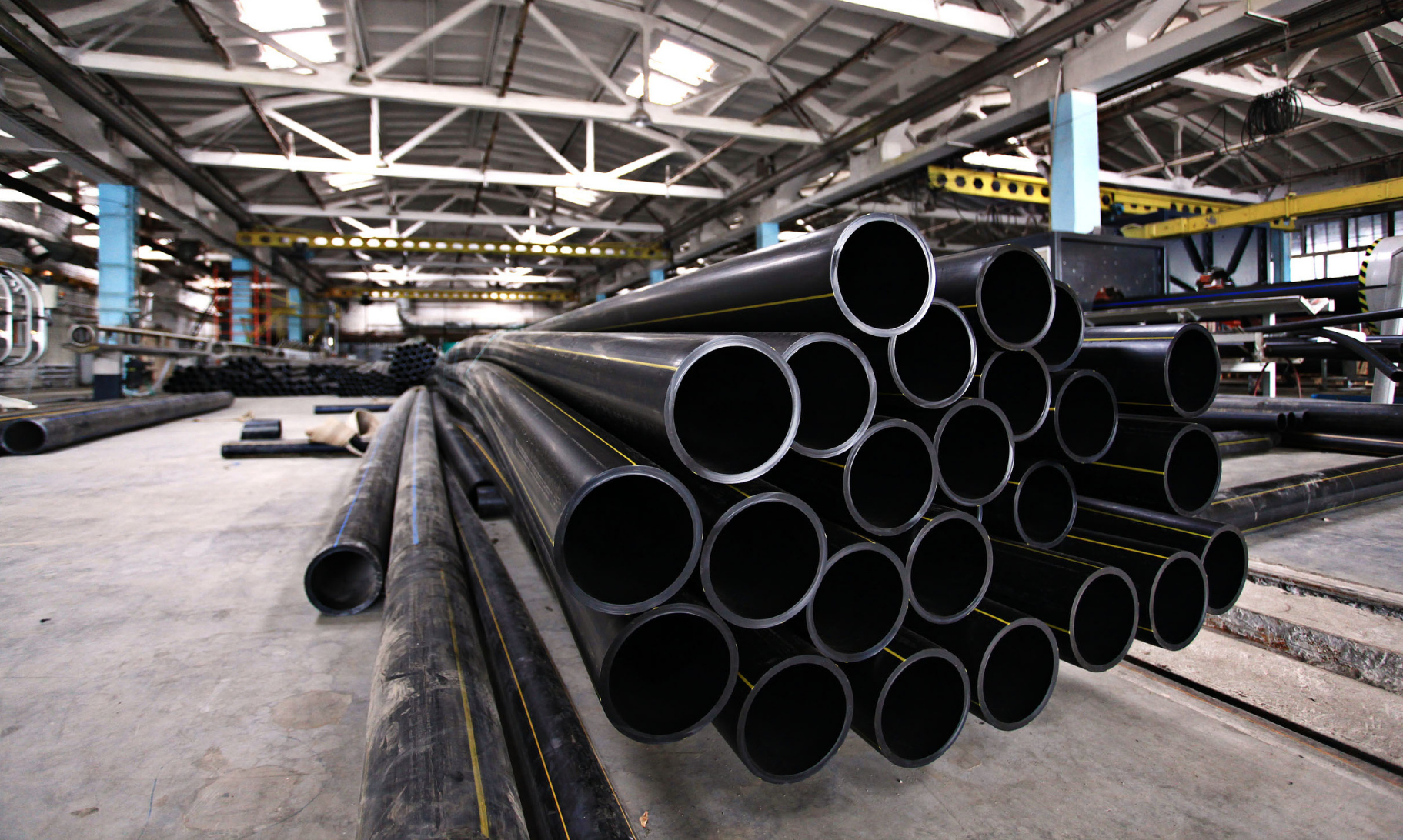 A bunch of black pipes are stacked on top of each other in a factory