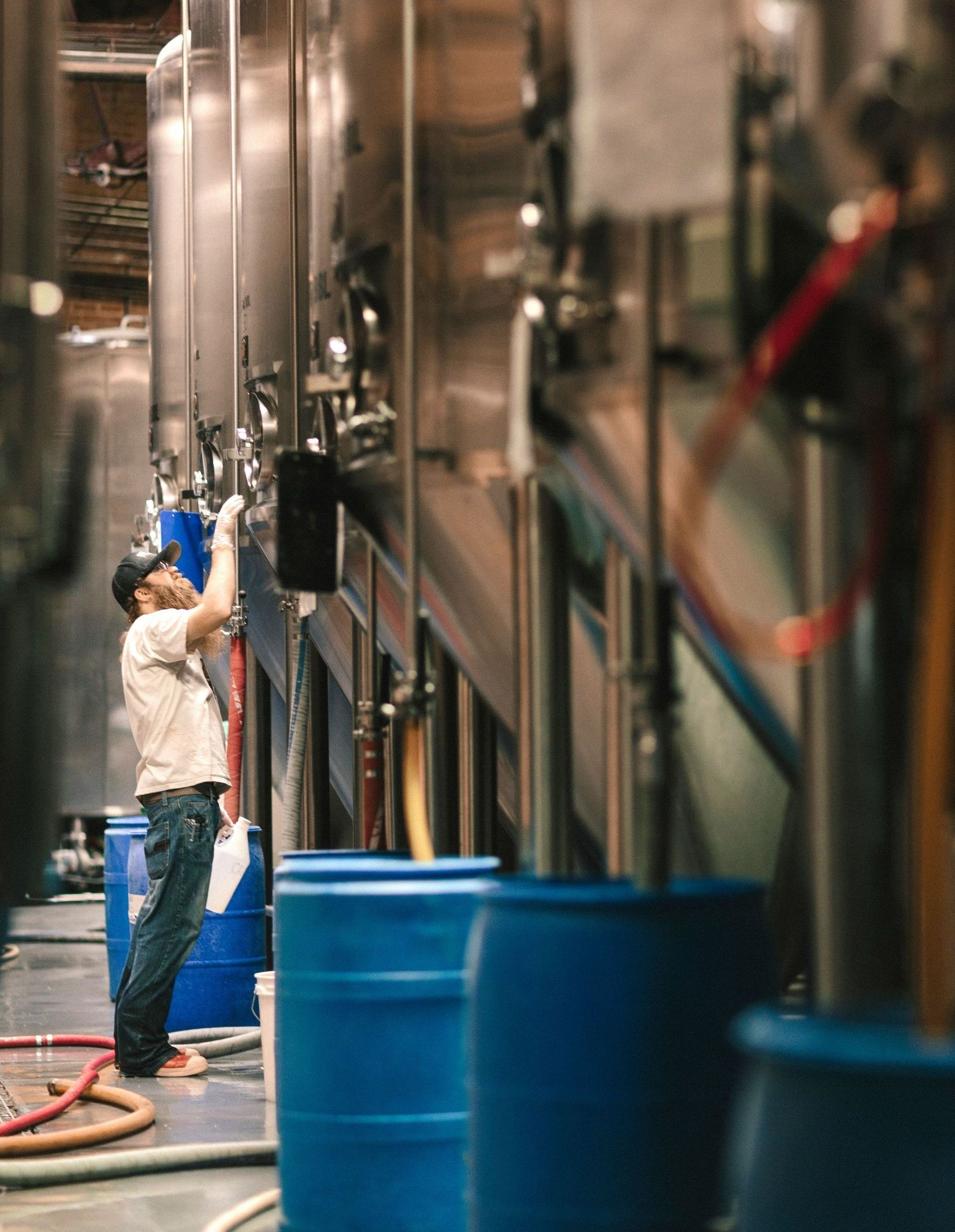 A man is working on a machine in a factory surrounded by blue barrels.