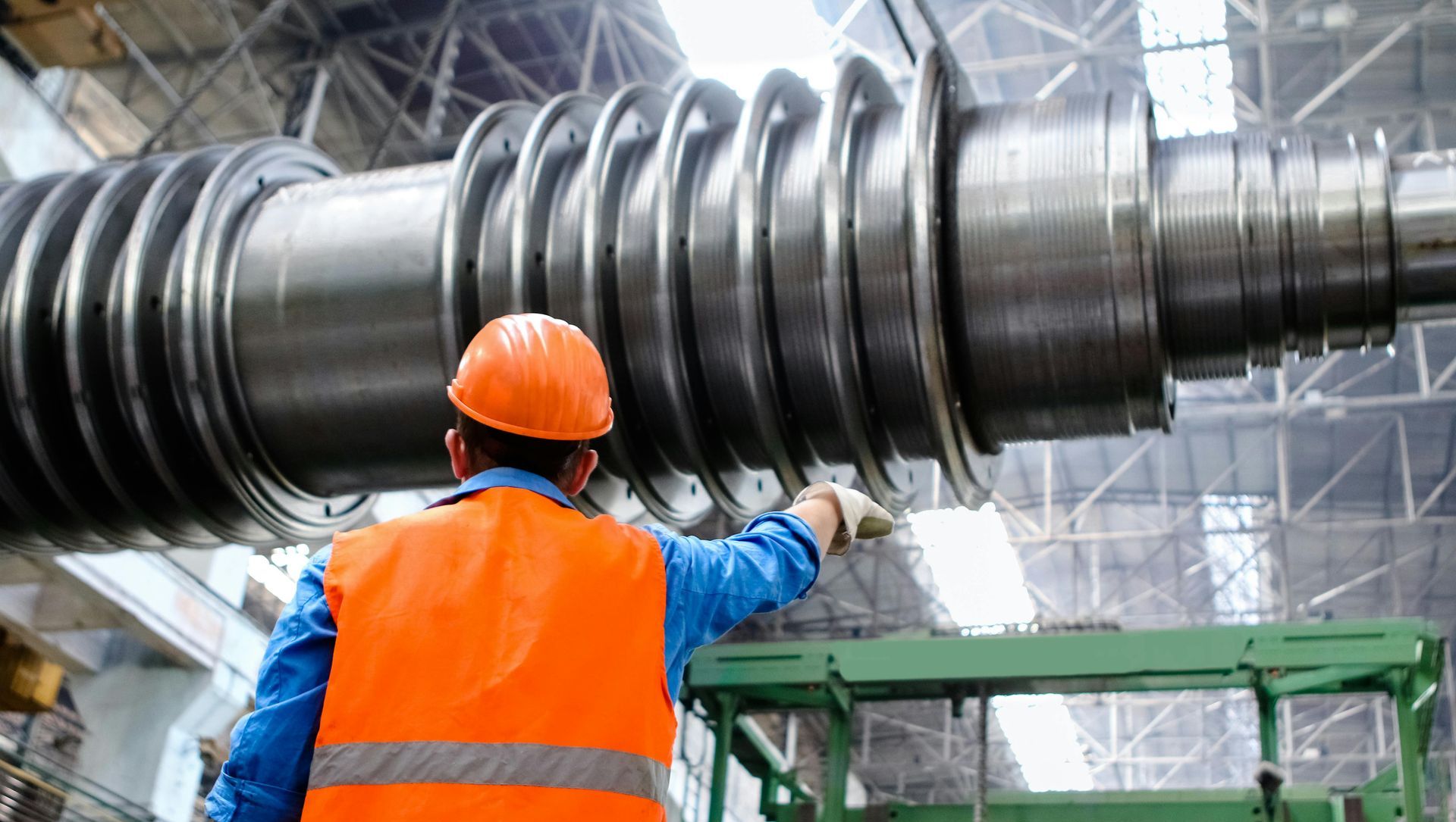 A man in an orange vest and hard hat is working on a large metal object.