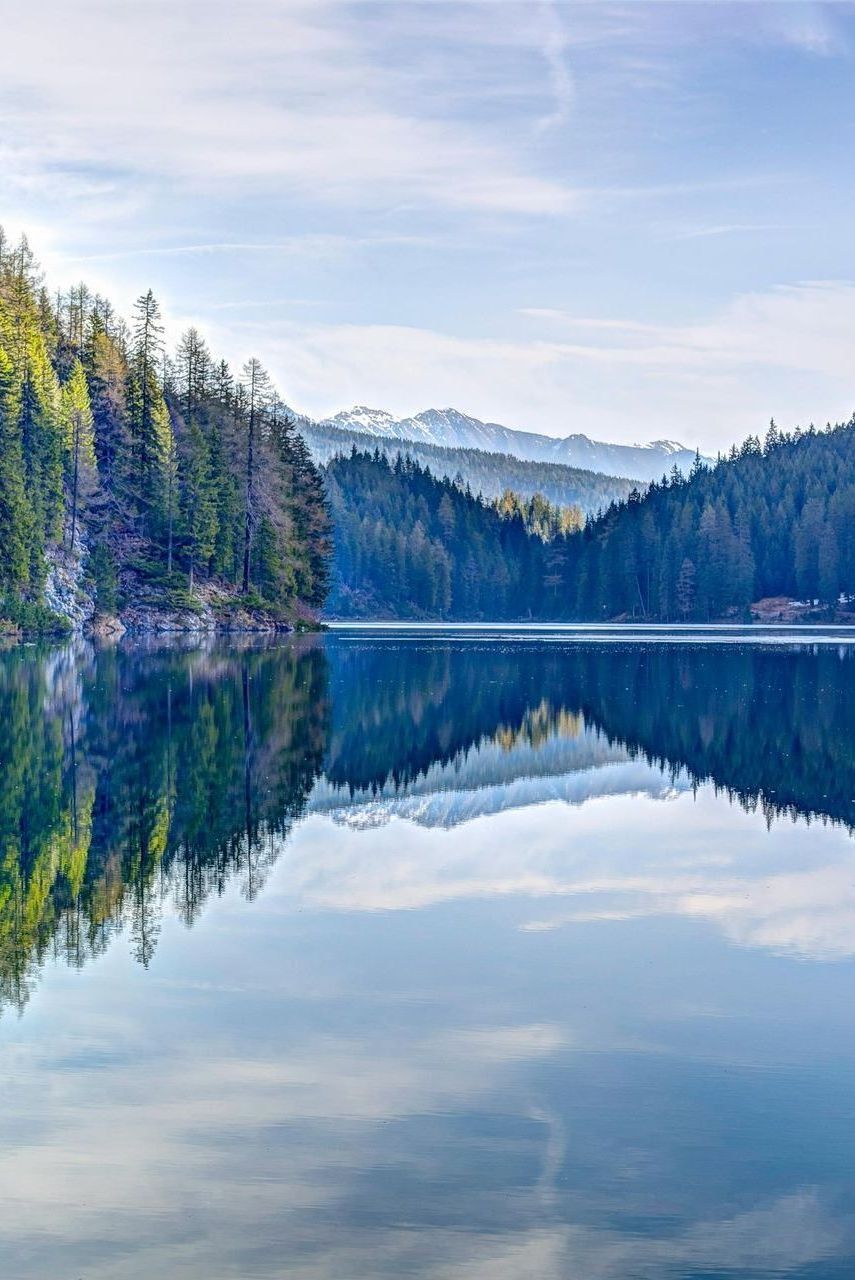 A lake surrounded by trees and mountains on a sunny day