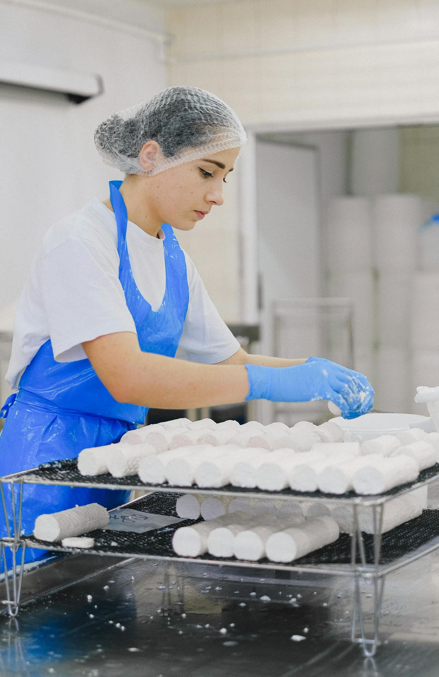 Woman in apron and gloves, making cheese in a commercial kitchen.