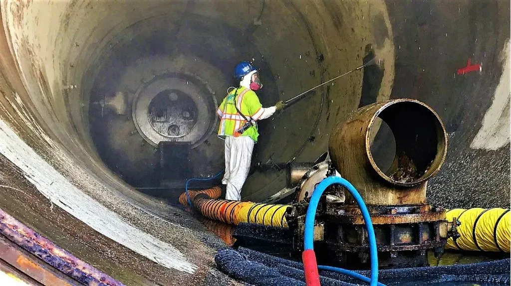 A man is cleaning a pipe in a tunnel with a hose.