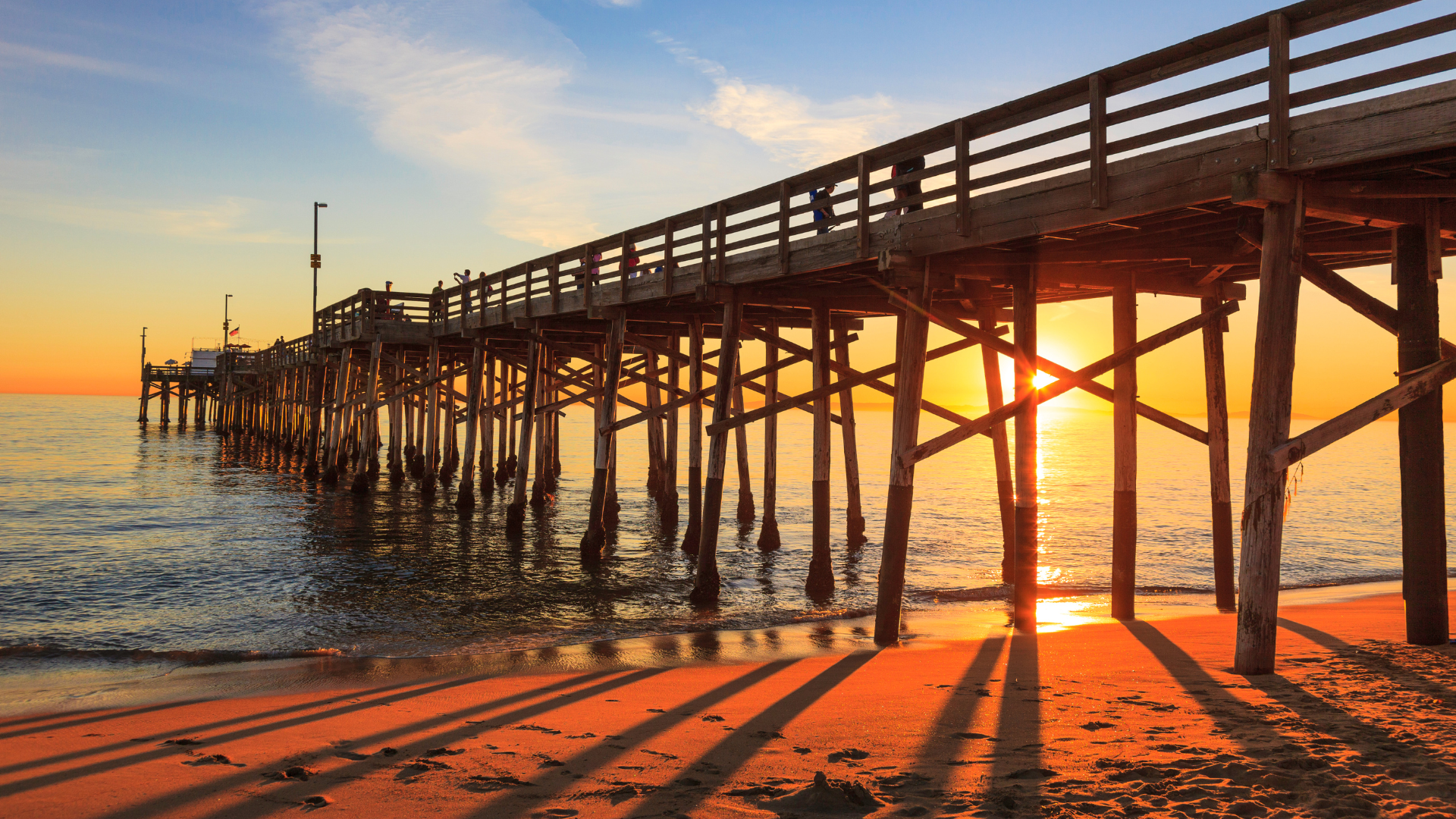 Wooden pier over ocean at sunset casting long shadows on the beach.