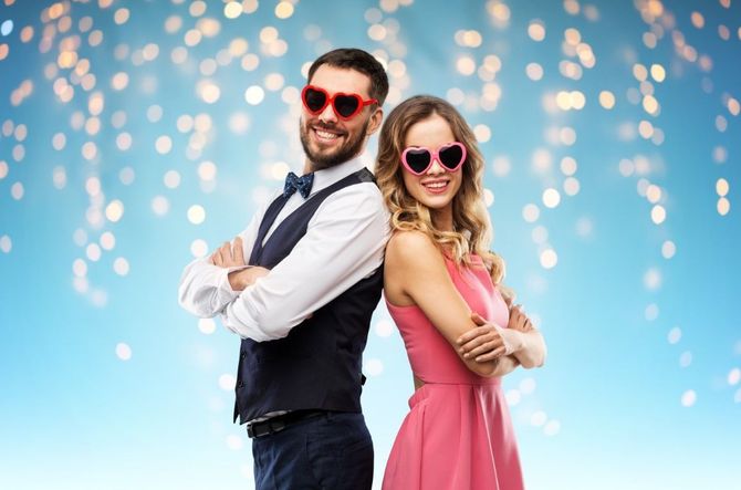 Two stylish people in sunglasses stand back-to-back, smiling against a blue background with glowing lights.
