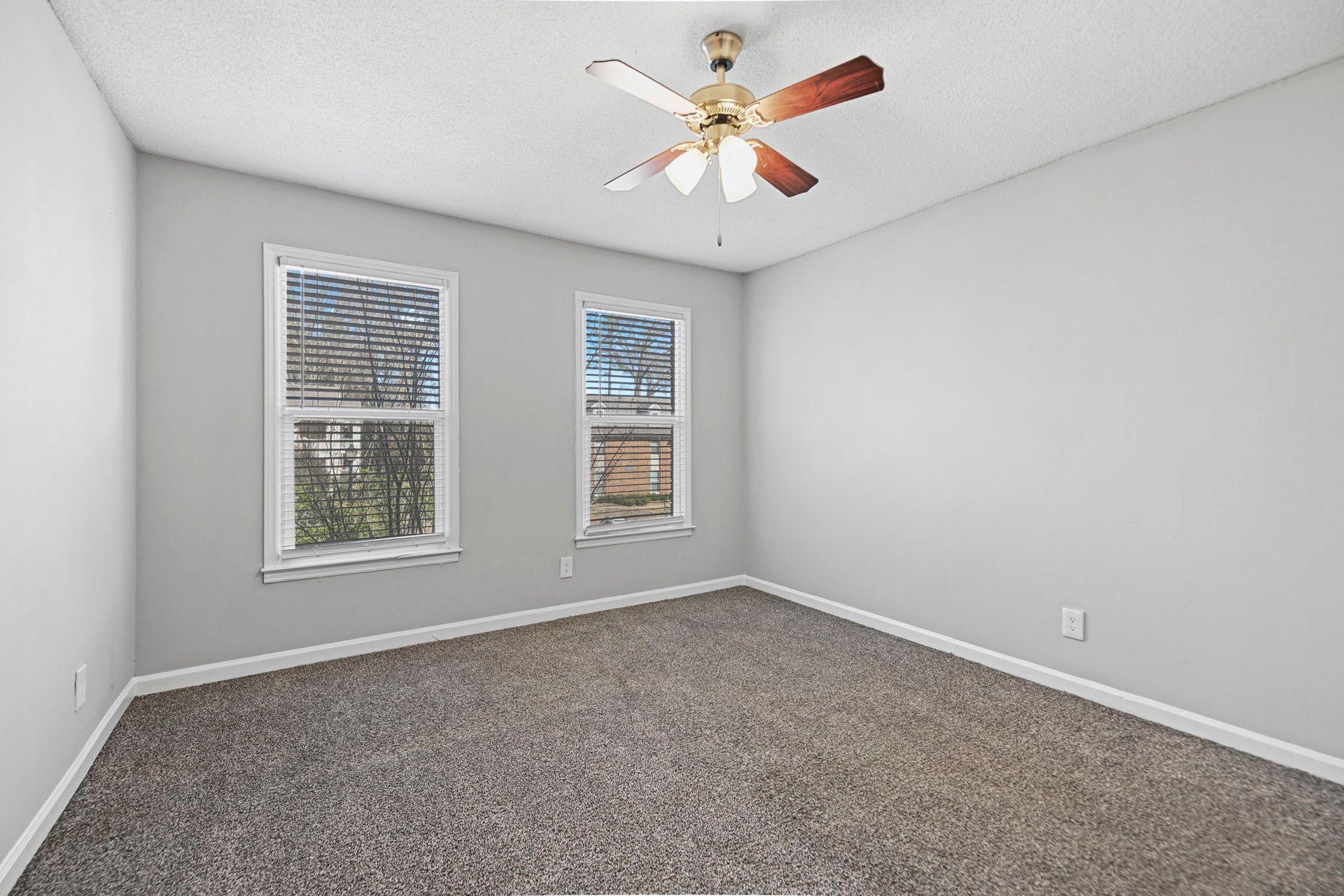 Empty room with gray walls, two windows, carpet flooring, and a ceiling fan.