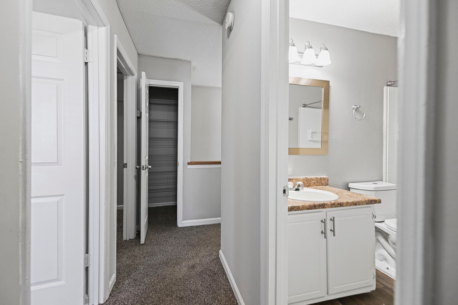 An interior view showing a carpeted hallway, a bedroom door, a linen closet, and a bathroom with a white vanity.