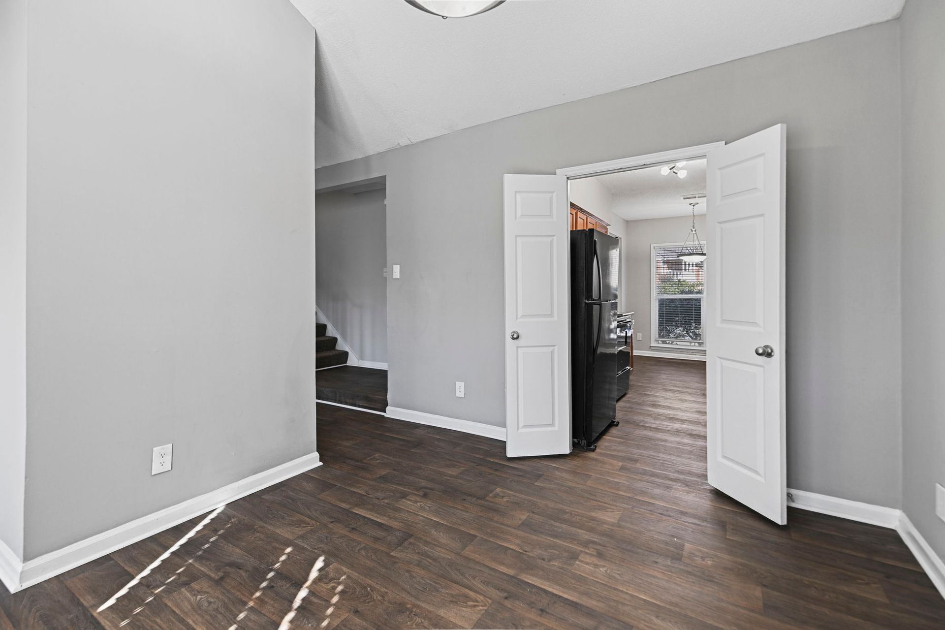 An empty room with gray walls and wood flooring, leading into an adjacent room through white double doors.