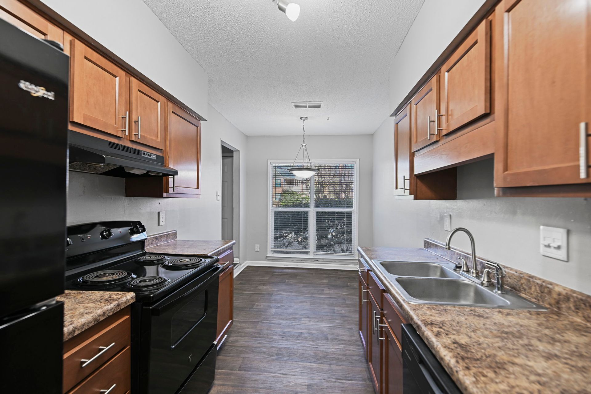 Galley kitchen with wood cabinets, brown countertops, black appliances, and a window view at the far end.