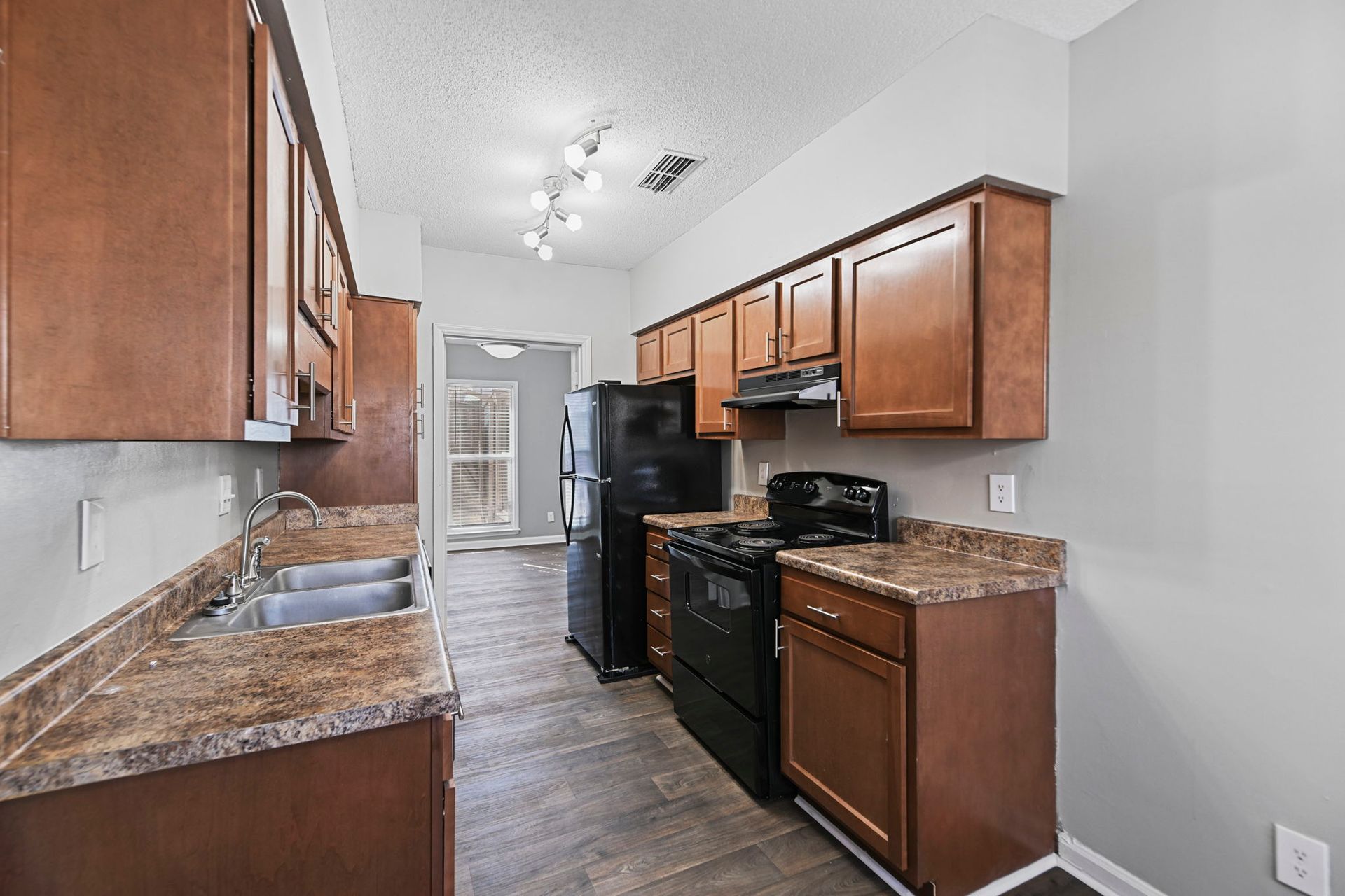 Galley kitchen with brown cabinets, wood-look floors, laminate countertops, and black appliances.