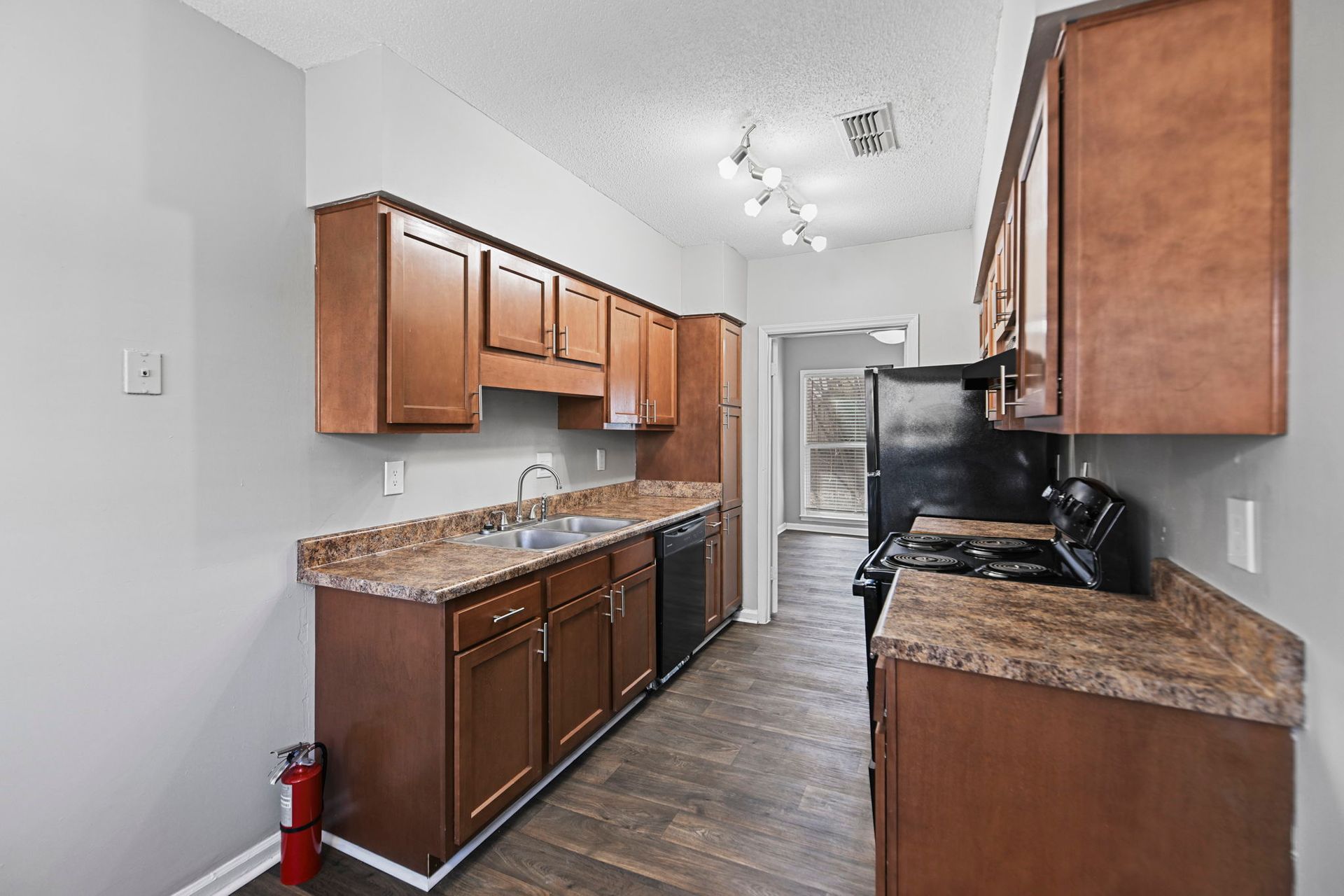 Kitchen with brown wood cabinets, mottled brown laminate countertops, black appliances, and gray walls.