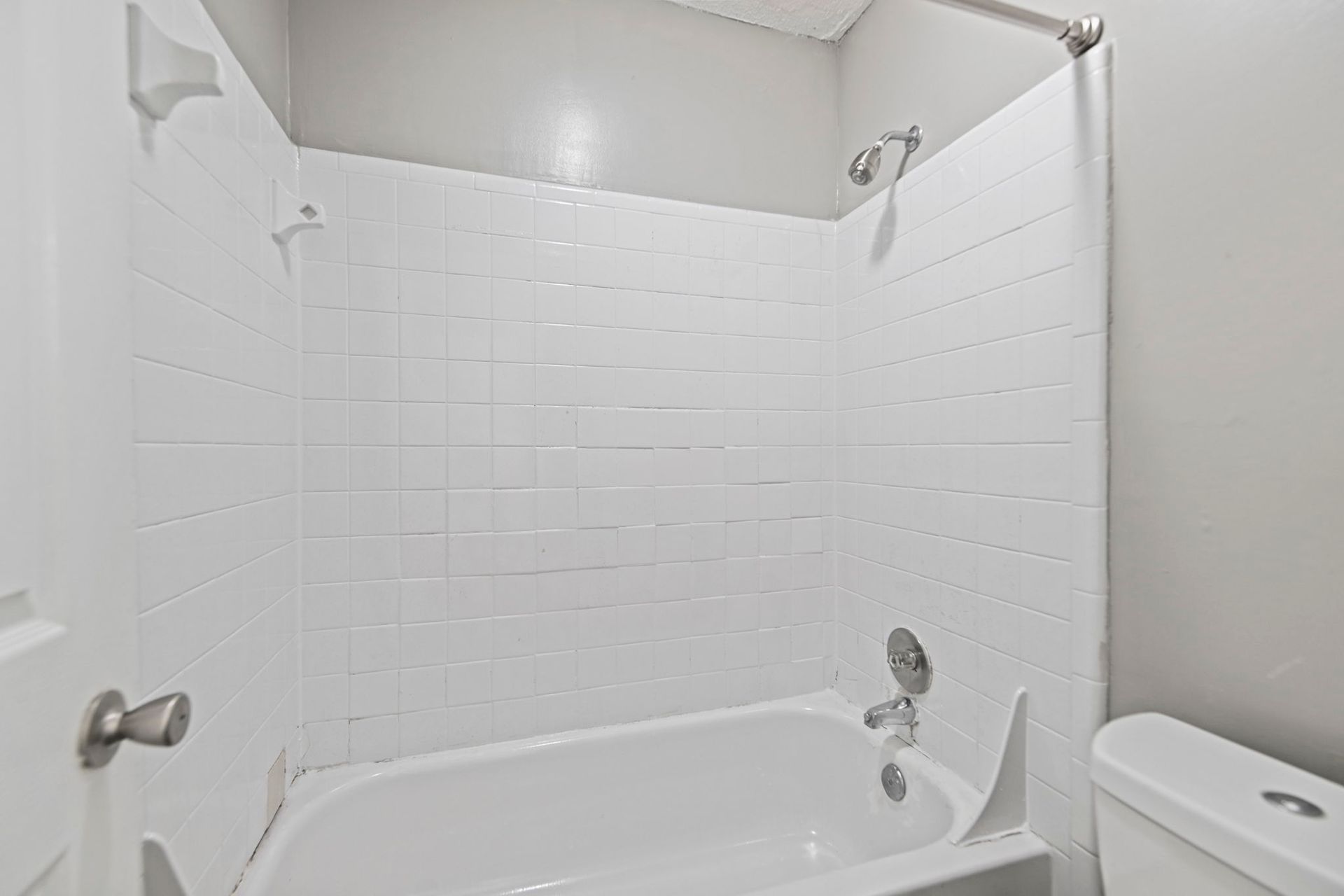 A white bathtub with a white subway-tile shower surround, showerhead, and faucet, adjacent to a white toilet.