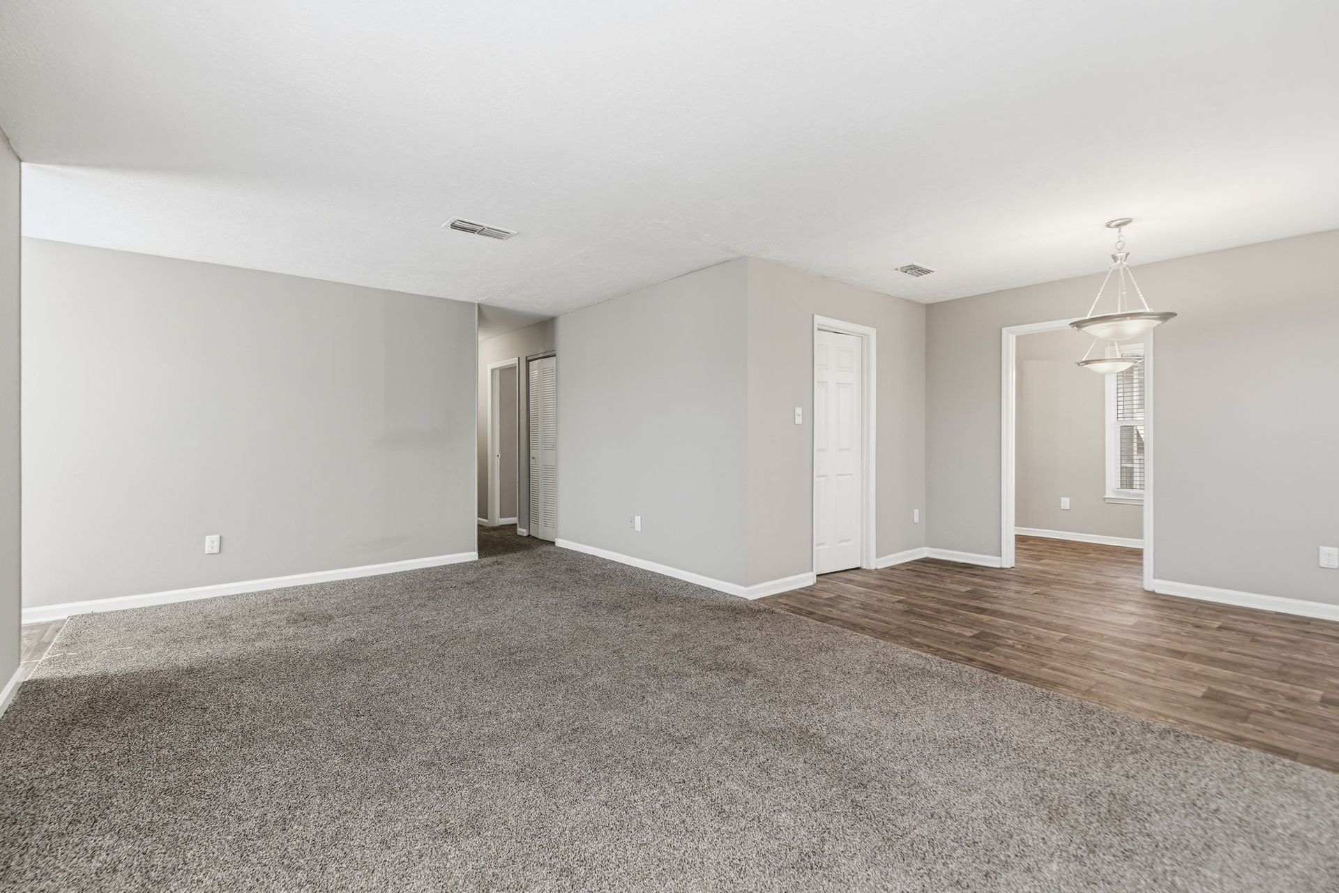 An unfurnished room featuring gray carpet transitioning to wood-look flooring, with light gray walls and a doorway.