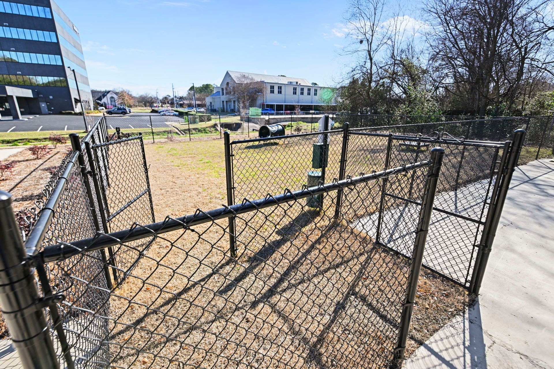 A fenced dog park area featuring a chain-link enclosure with a small, raised shelter structure in the background.