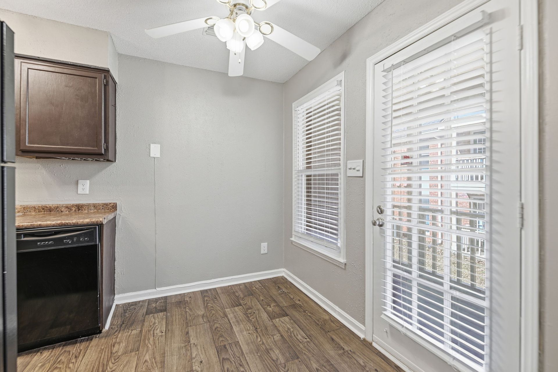 A brightly lit kitchen corner with light gray walls, wood-look flooring, a dark cabinet, and a door with glass panes.