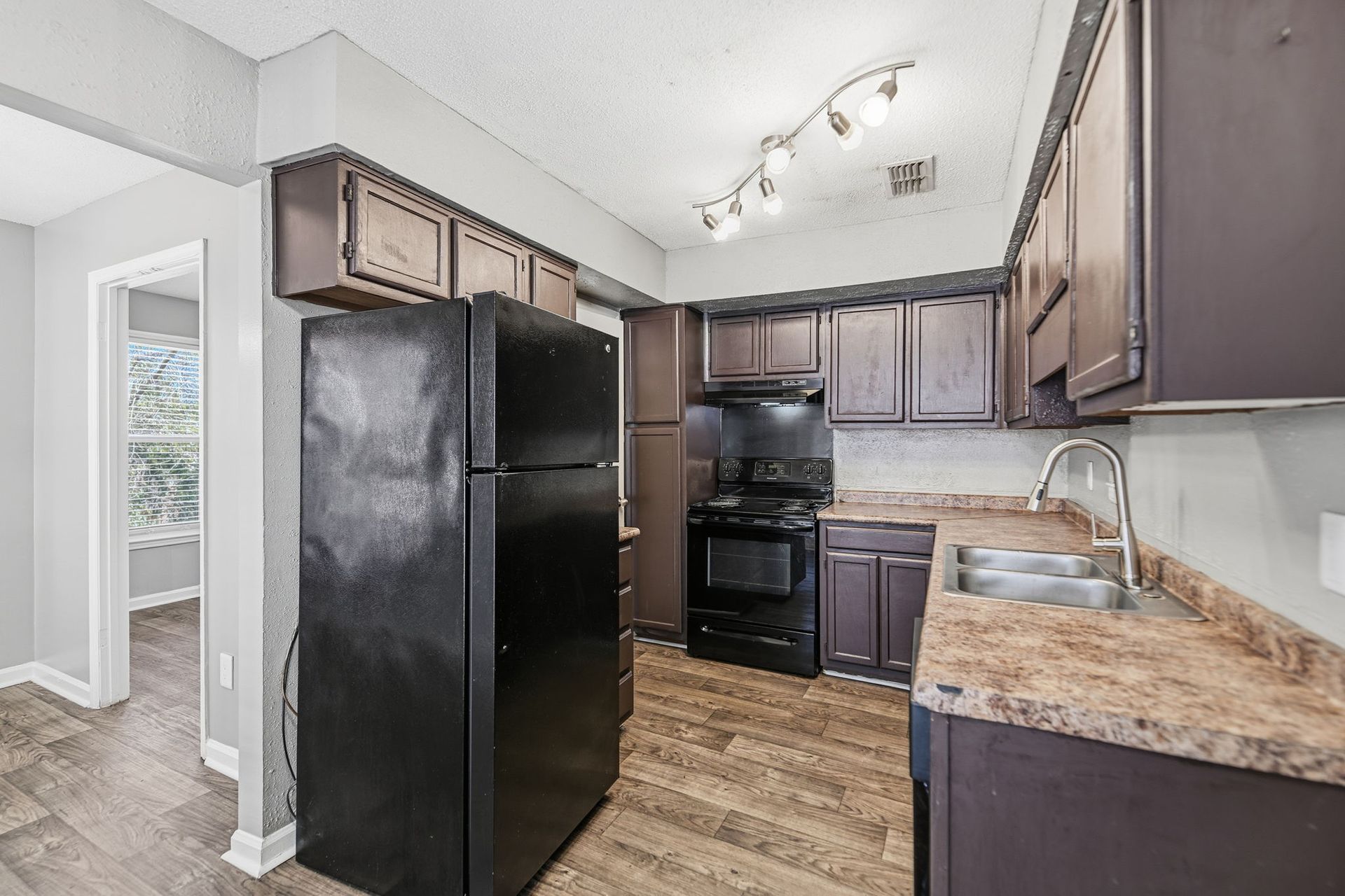 Kitchen with dark wood cabinets, black appliances, speckled laminate countertops, and light gray walls.