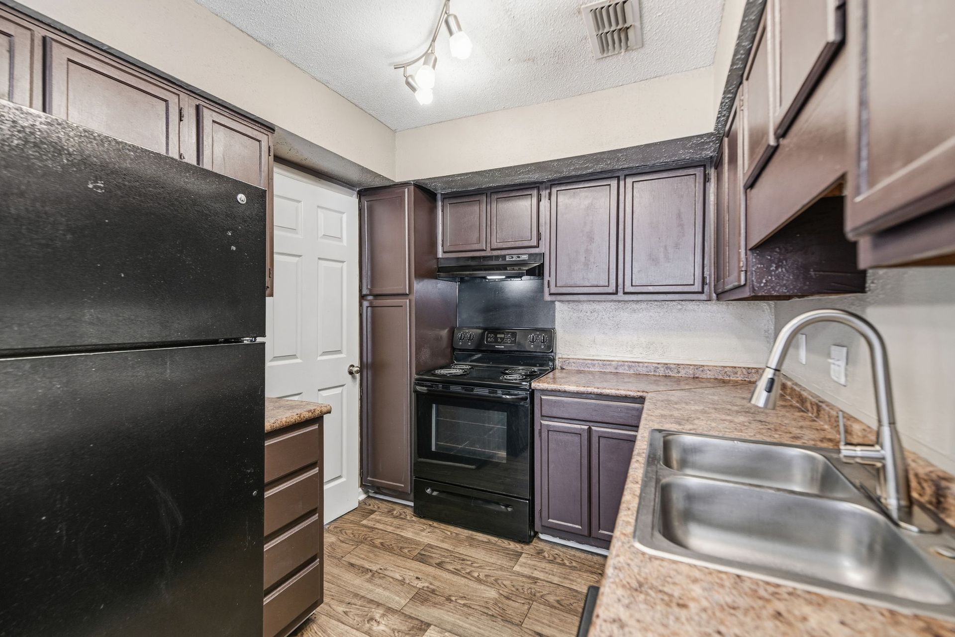 A kitchen with dark cabinets, black appliances, a double sink, and light-colored laminate countertops.
