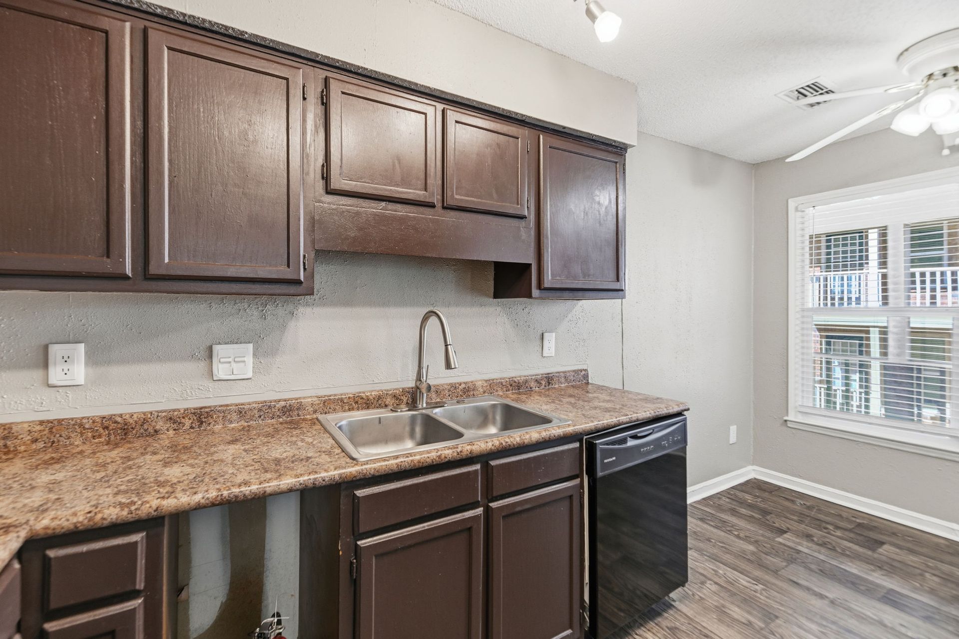 A kitchen featuring dark wood cabinets, a speckled laminate countertop, a stainless steel sink, and a black dishwasher.