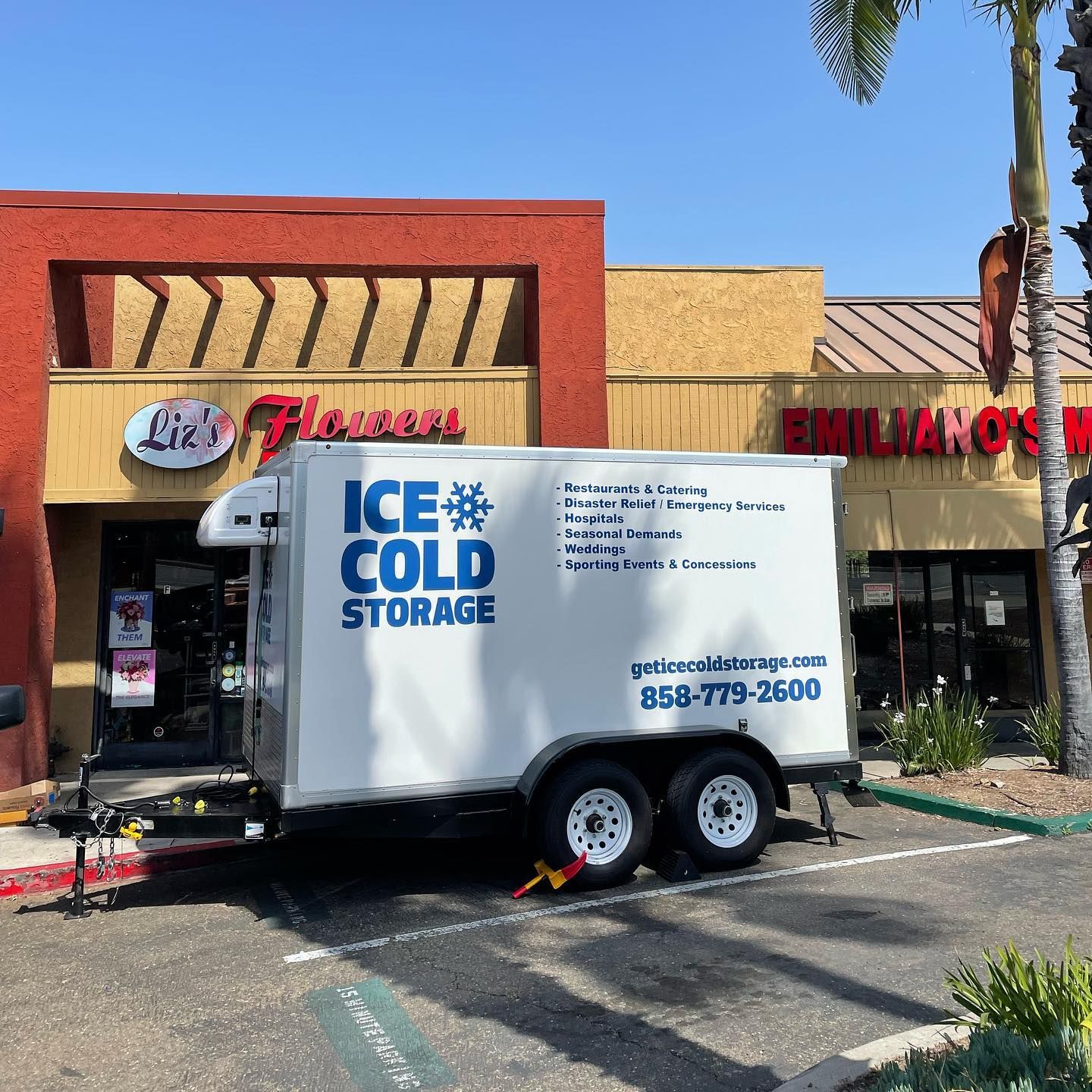 An ice cold storage trailer is parked in front of a building