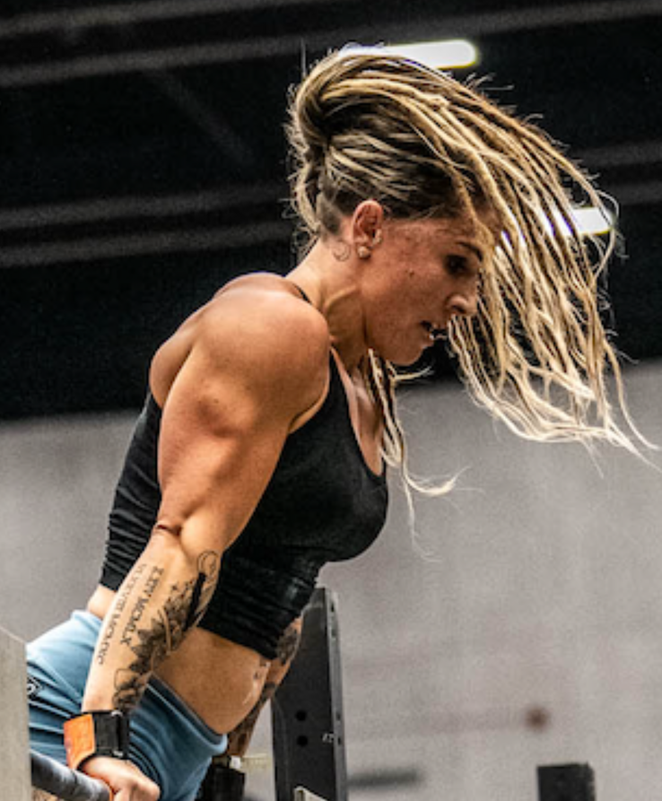 Athlete with dreadlocks performing a bar dip, showing intense focus in a gym setting.