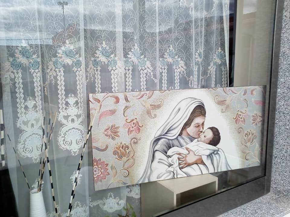 Su una finestra è appeso un dipinto raffigurante una donna che tiene in braccio un bambino.