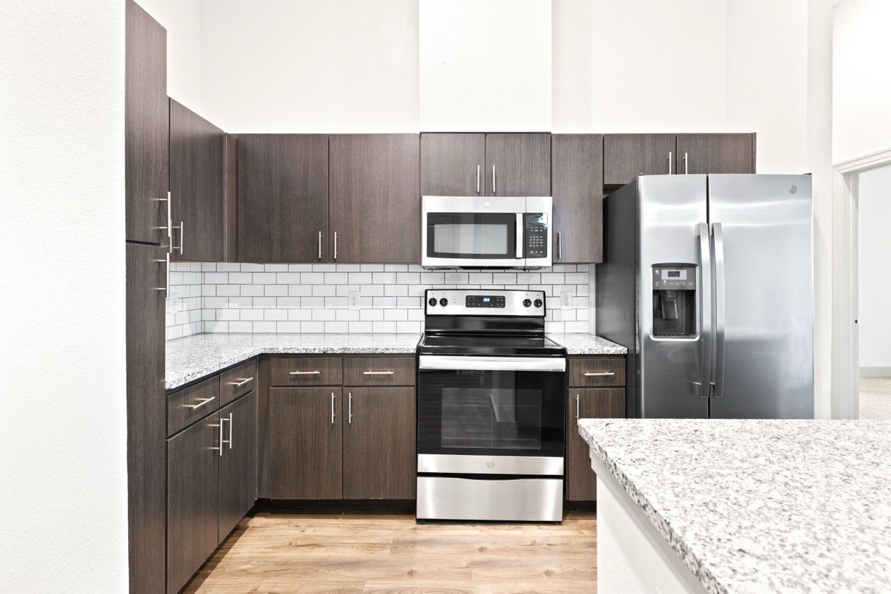 Modern apartment kitchen with dark wood cabinets, stainless steel appliances, and granite countertops at Olympus Hudson Oaks.