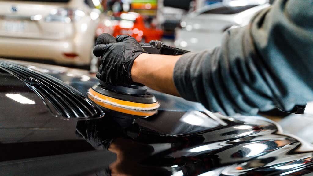 A man is polishing the hood of a black car.