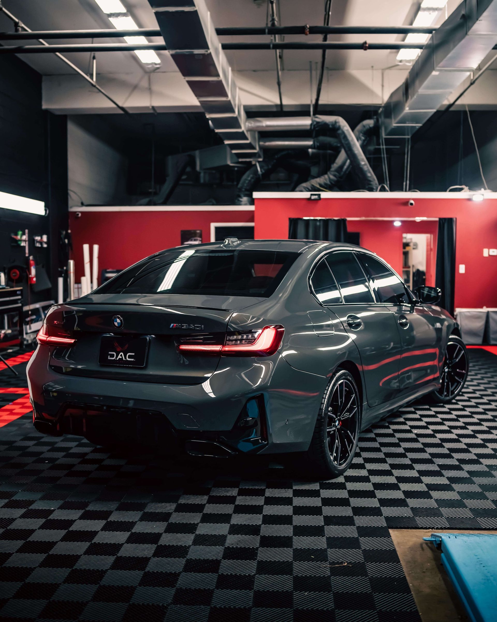 A gray car is parked in a garage with a checkered floor.