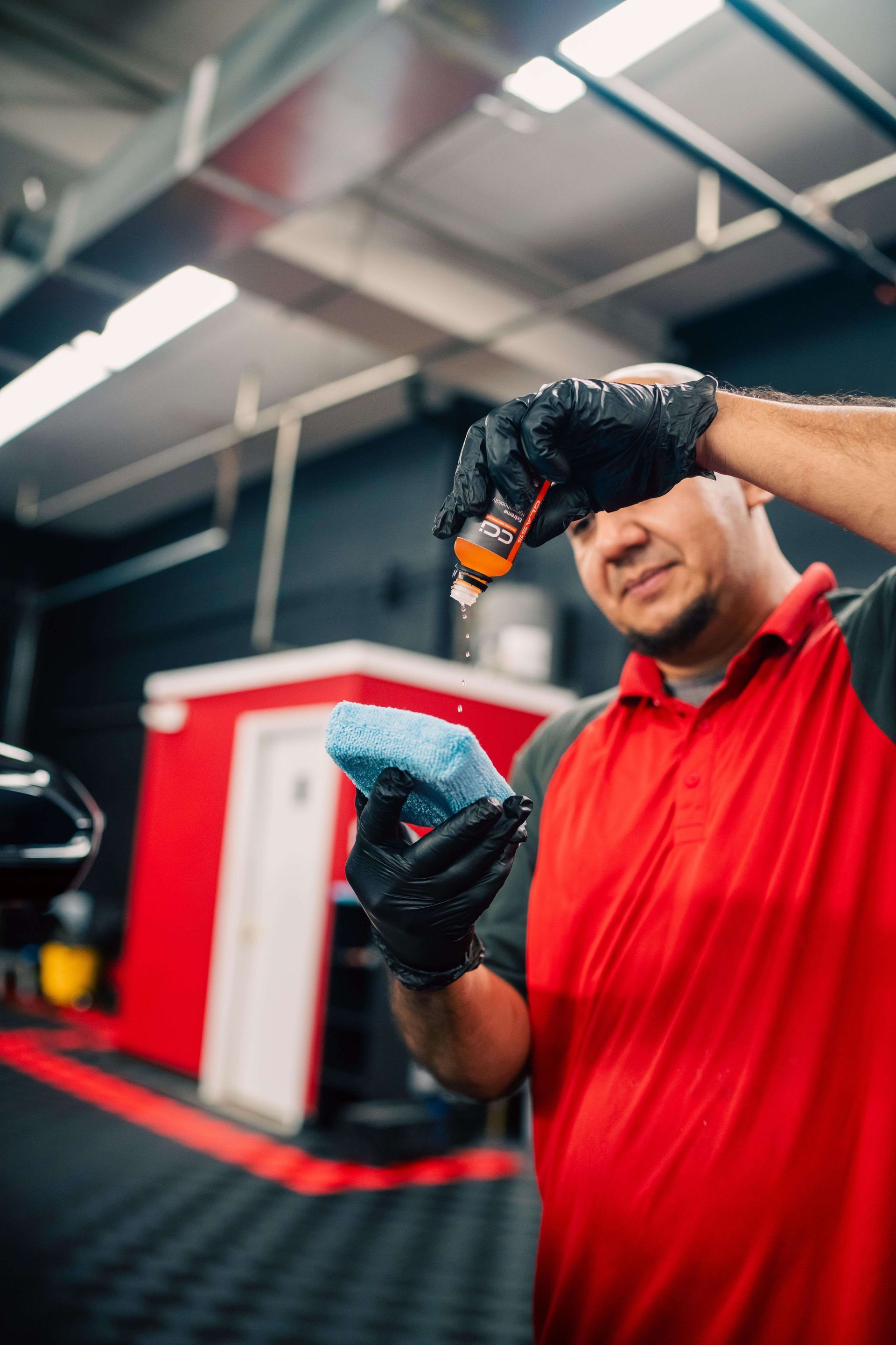 A man in a red shirt and black gloves is applying a coating to a car.