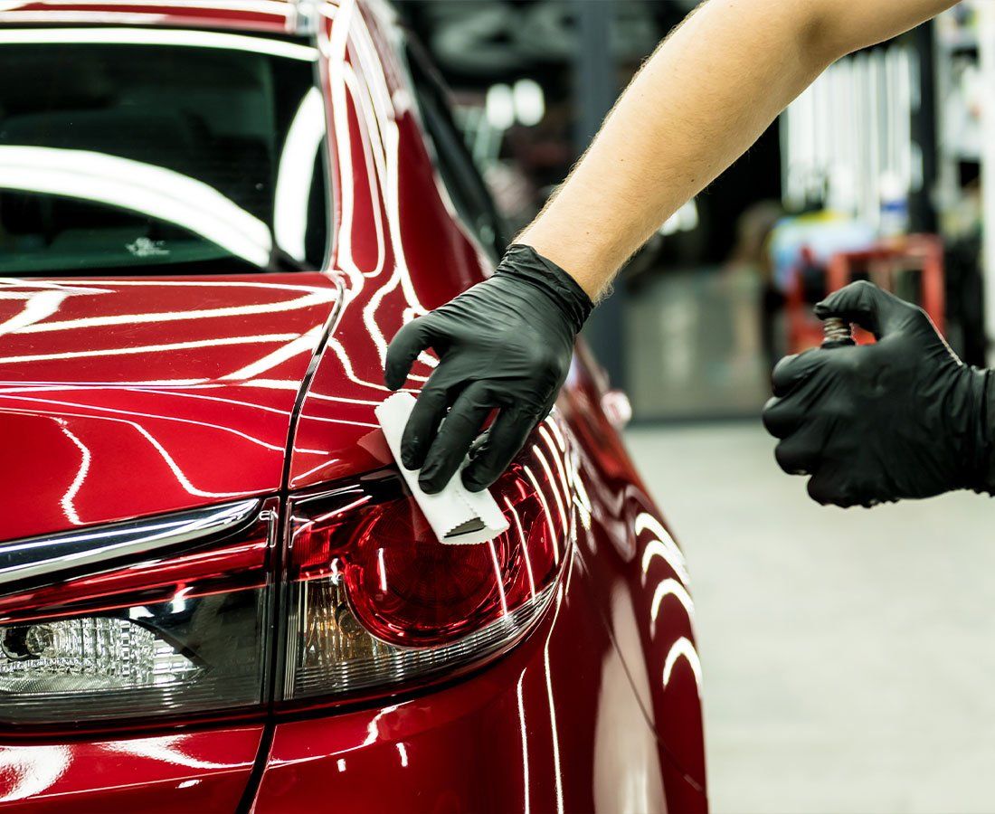 A person wearing black gloves is polishing a red car.