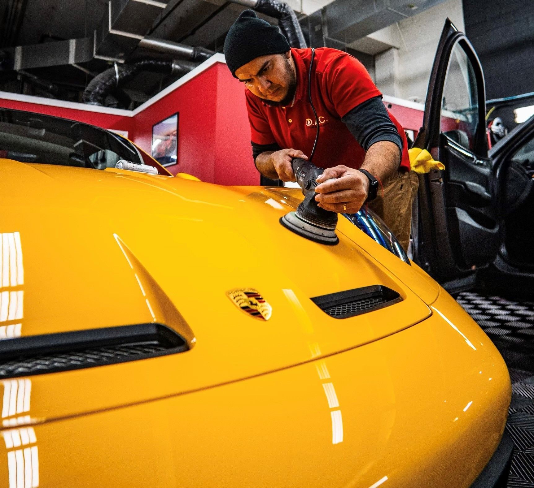 A man is polishing the hood of a yellow sports car.