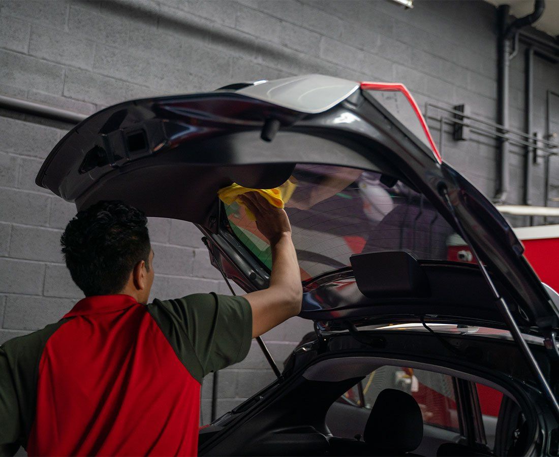 A man in a red shirt is opening the trunk of a car