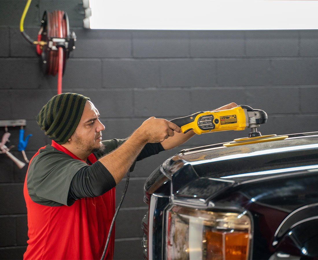 A man is polishing the hood of a black truck.