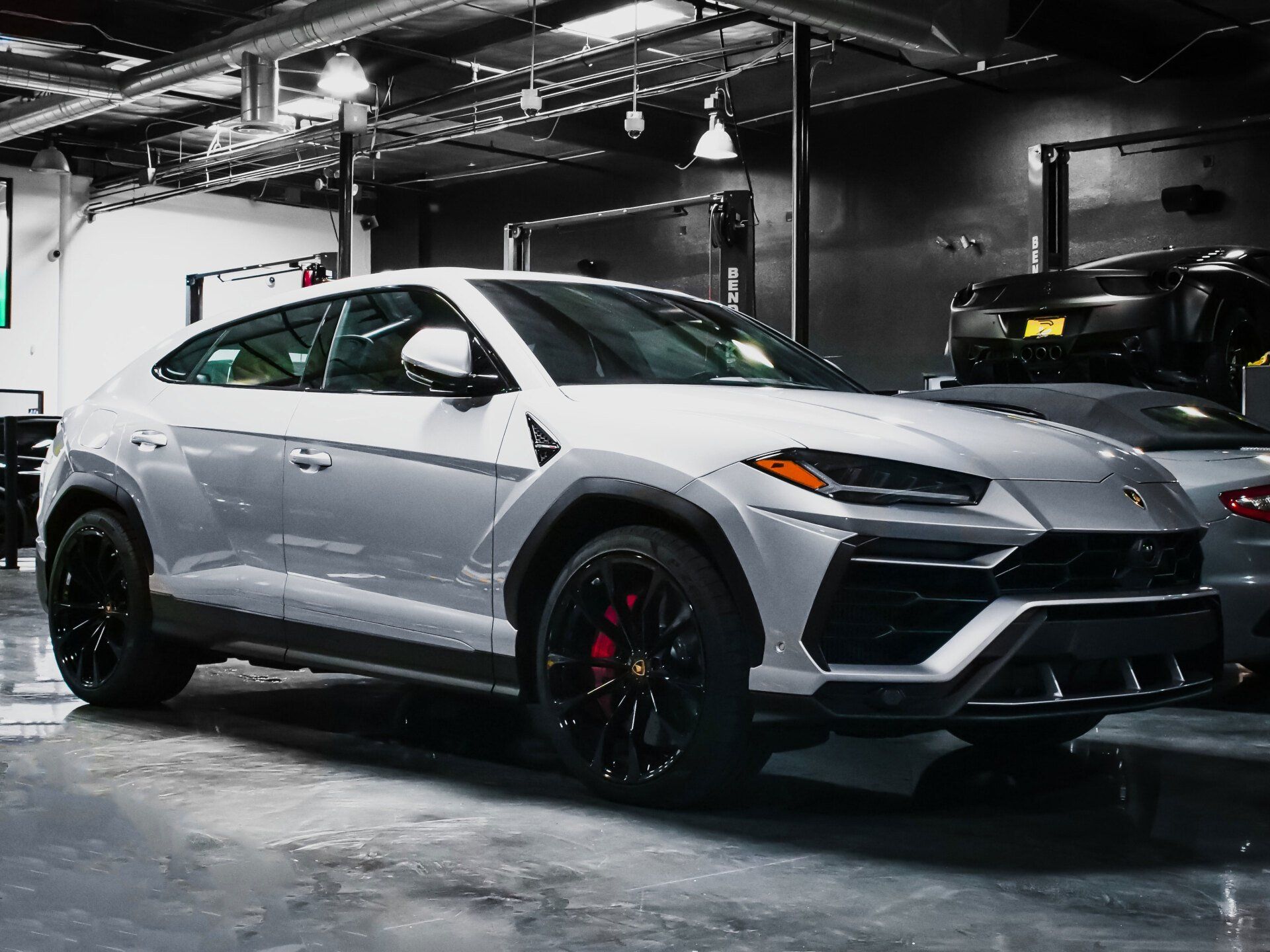 A silver lamborghini urus is parked in a garage.