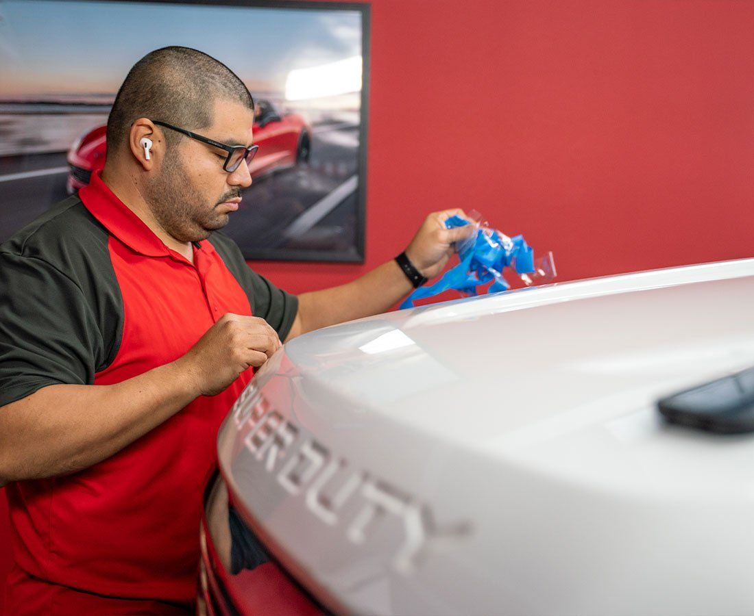 A man in a red shirt is working on the hood of a car.