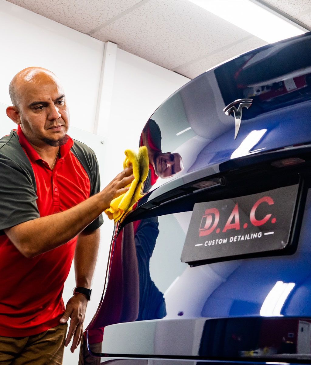 A man in a red shirt is cleaning a blue car with a yellow cloth.