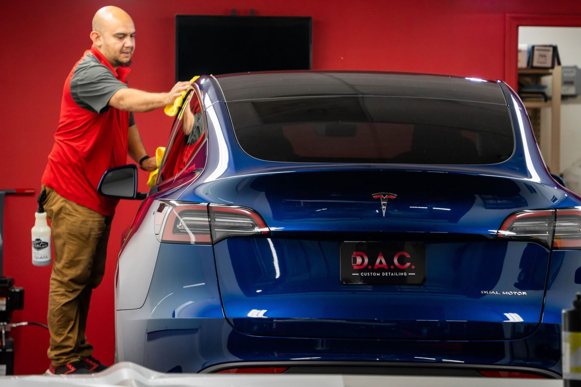 A man is cleaning the windshield of a blue tesla model s in a garage.