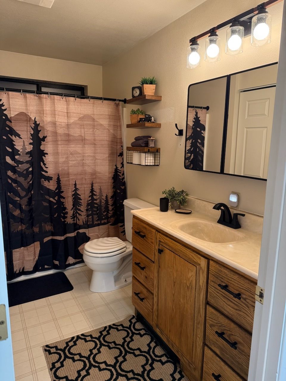 Bathroom with wood vanity, mirror lights, shower curtain, toilet, and patterned rug.