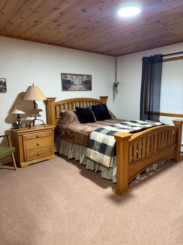 Bedroom with wooden bed, nightstands, lamp, and window with dark curtains on beige carpet.