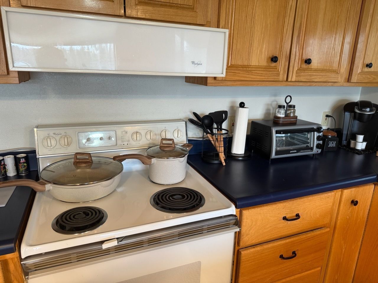 Kitchen counter with stove, toaster oven, utensils, and cookware on a black countertop