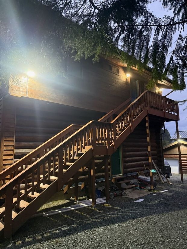 Snow-covered log cabin at dusk with wooden stairs and warm exterior lights