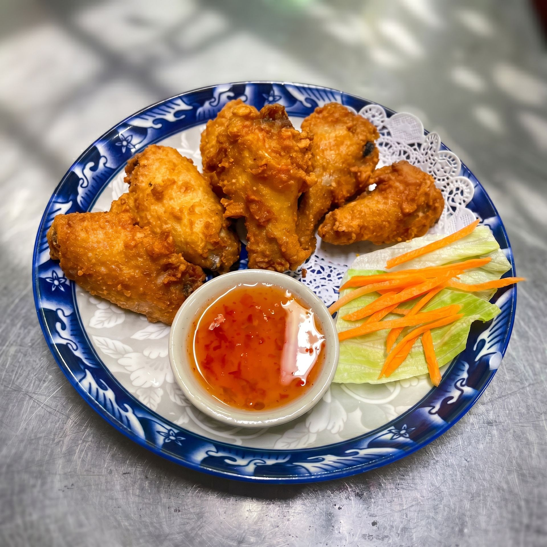 Plate of fried chicken wings with dipping sauce and carrot sticks on a blue-rimmed dish