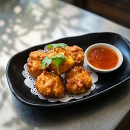 Golden fried dumplings on a black platter with red dipping sauce and cilantro garnish