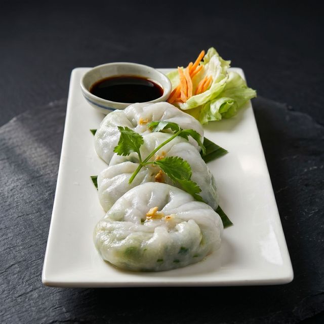 Steamed shrimp dumplings on a white plate with soy sauce and pickled vegetables on the side