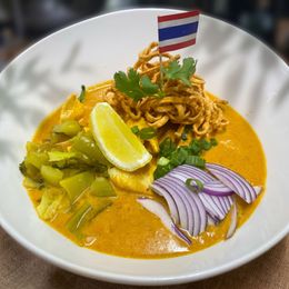 Thai curry noodles with tofu, lime wedge, herbs, and sliced red onion in a white bowl on a table