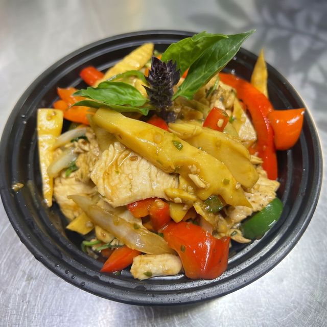 Black bowl of mixed stir-fry with chicken, red peppers, basil, and yellow vegetables on a metal surface