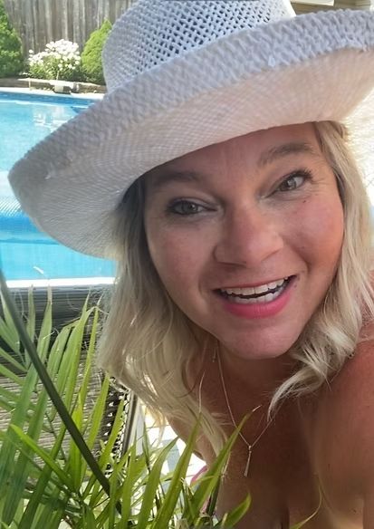A woman wearing a white hat is smiling in front of a pool.