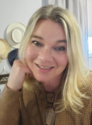 A woman wearing glasses and a brown sweater is smiling for the camera.