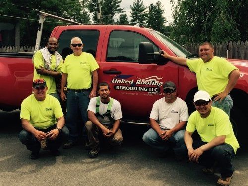 Seven people in neon shirts posing in front of a red service truck outdoors