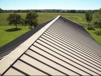 Metal roof ridge with solar panels beside a green field under a clear sky
