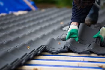 Worker installing dark roof tiles with green gloves on a sloped roof
